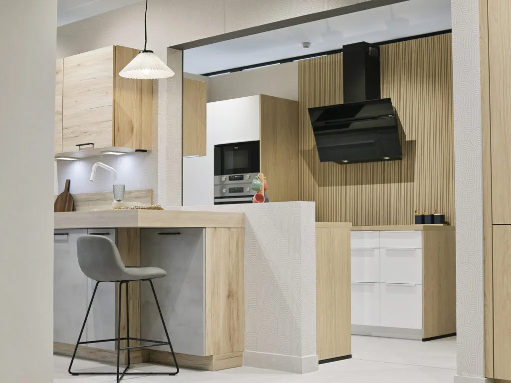 Cocina expuesta con muebles de madera clara, campana negra y taburete en el showroom
