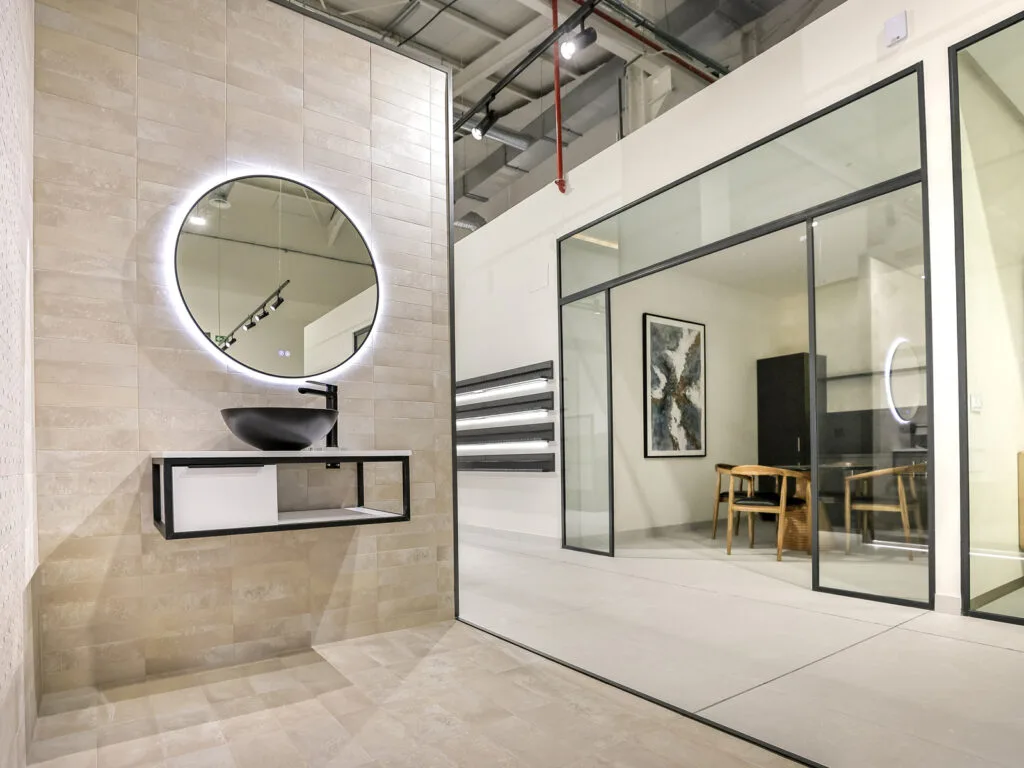 Ambiente de baño con espejo redondo iluminado y despacho acristalado en el showroom