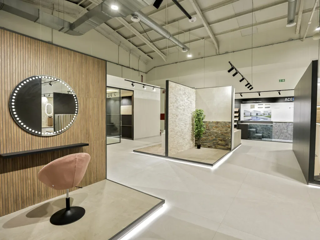 Zona de exposición con espejo iluminado, sillón rosa y ambientes de baño