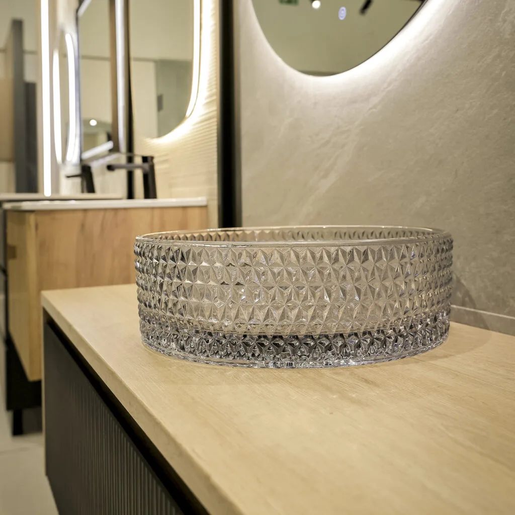 Lavabo de vidrio tallado sobre encimera de madera con espejo iluminado