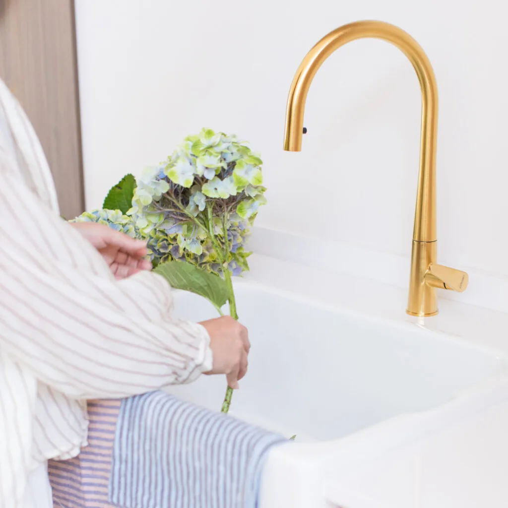 Grifo de cocina dorado sobre fregadero cerámico blanco con flores