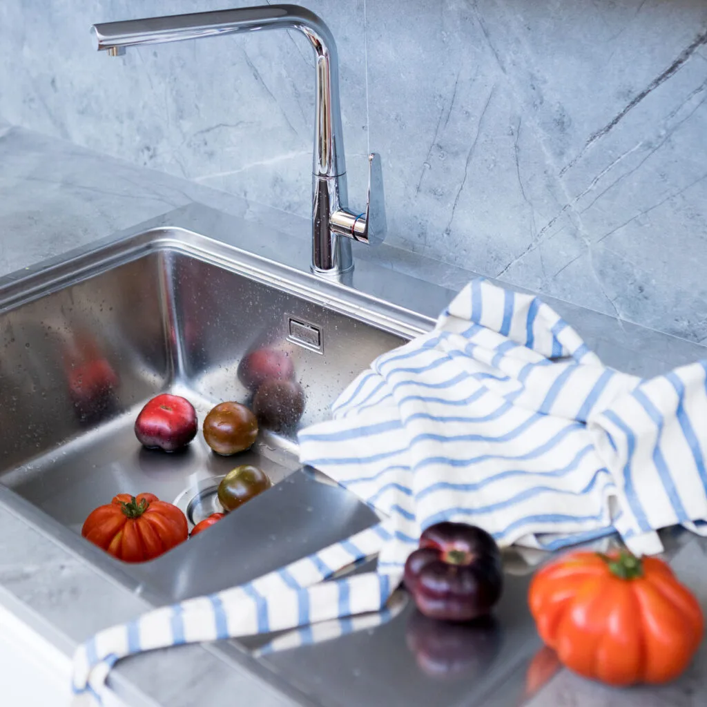 Fregadero de acero con tomates, paño de rayas y encimera de mármol