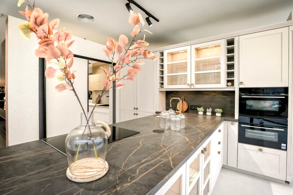 Cocina blanca con vitrinas y encimera oscura veteada con ramo de flores