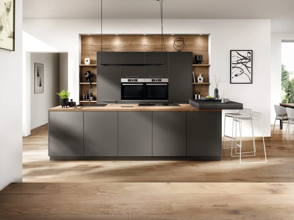 Cocina con isla gris mate, columnas de hornos y nicho de madera iluminado